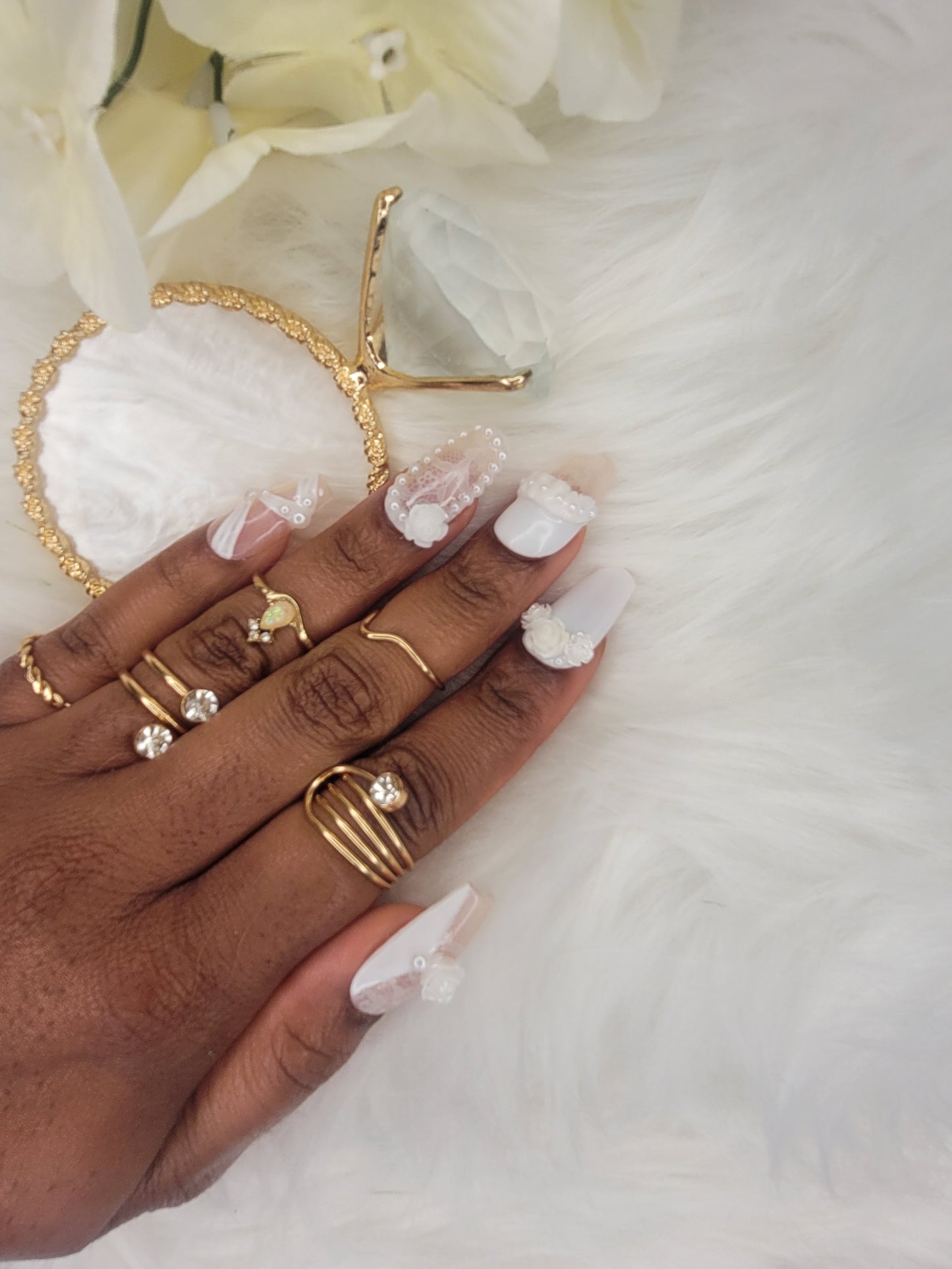 Hand wearing gold rings with white nail polish against a soft white background