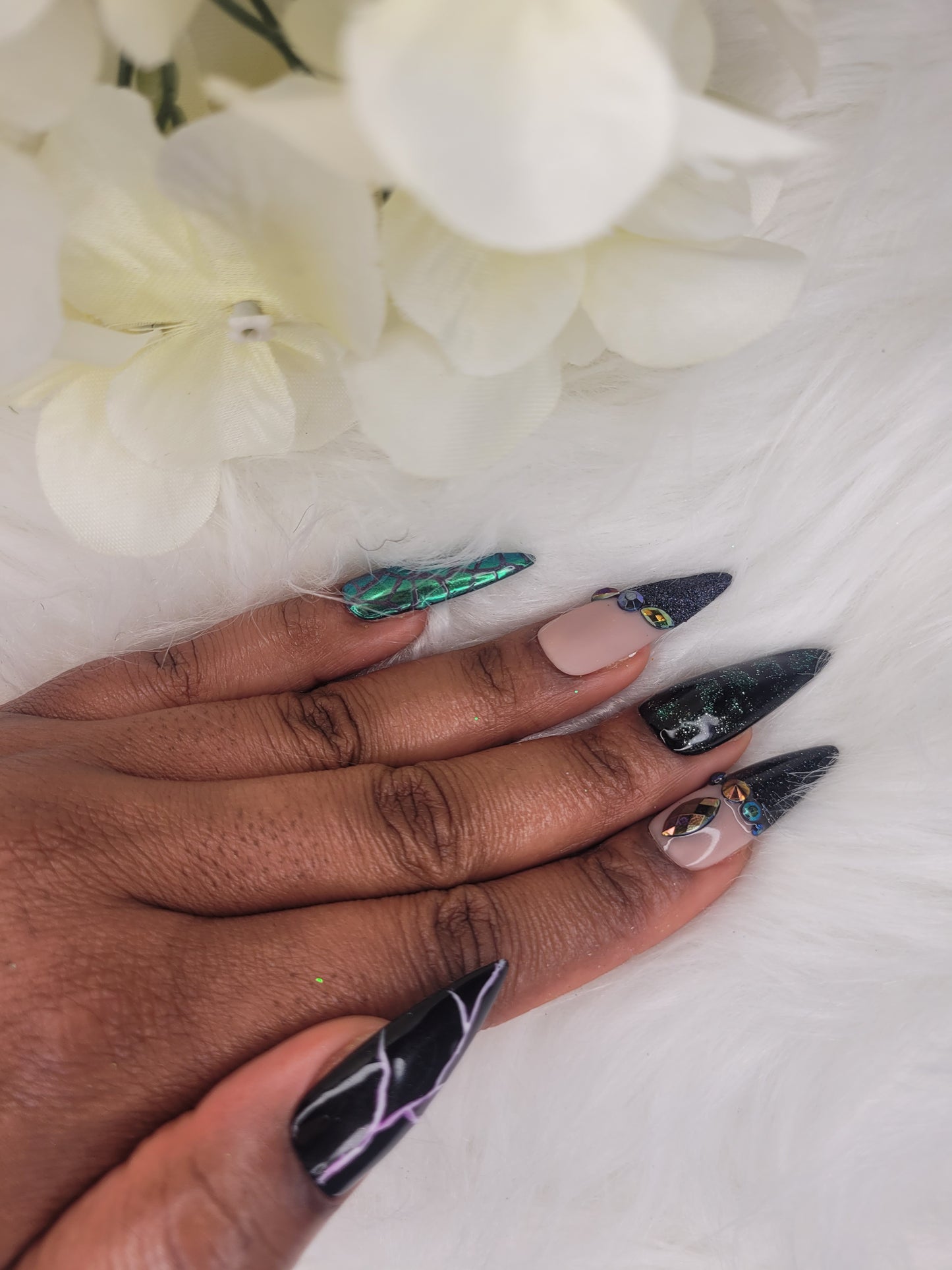 Hand with long, decorated nails against a white background with flowers.