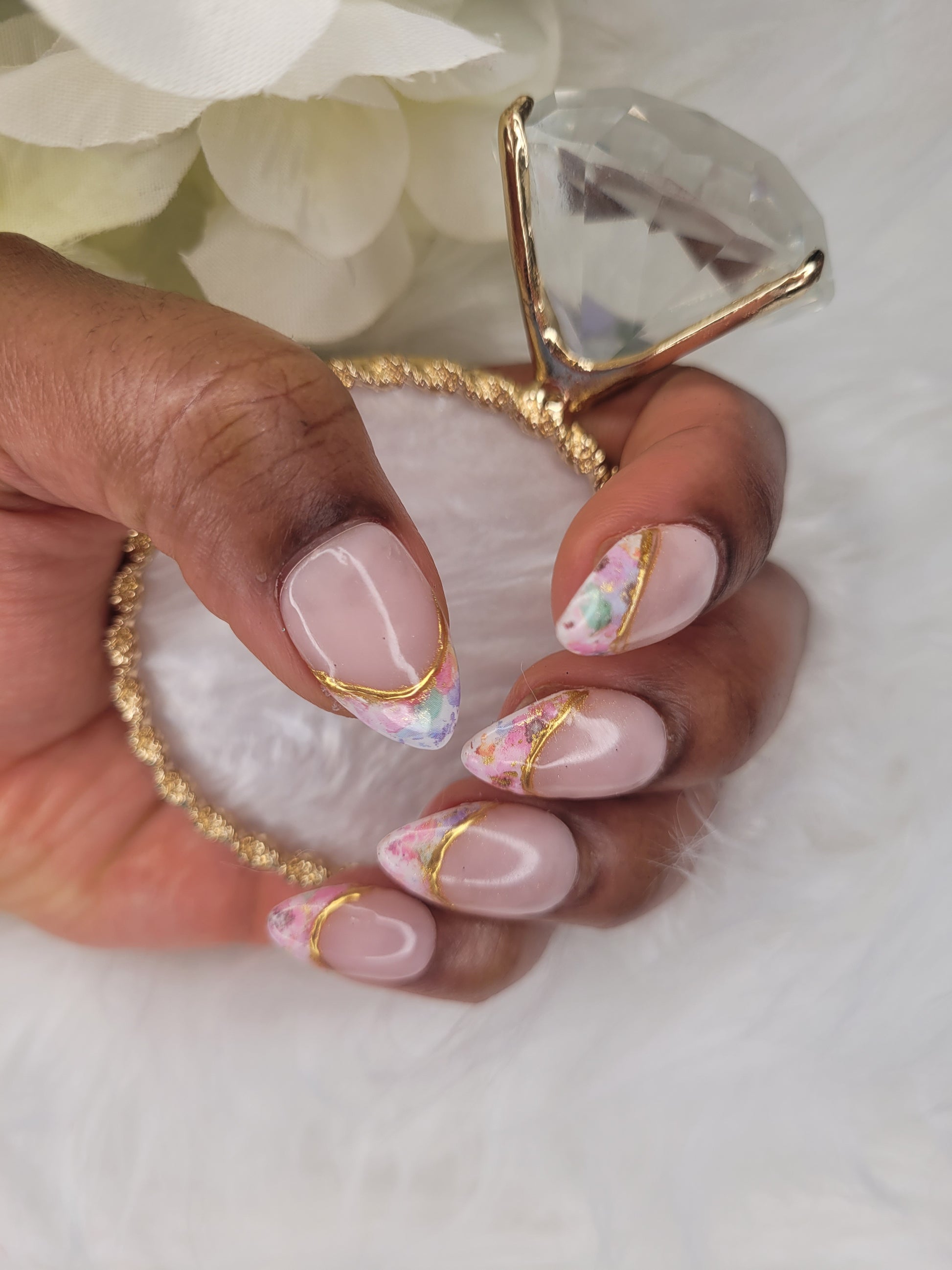 Hand with pink and gold nail design holding a decorative ring.
