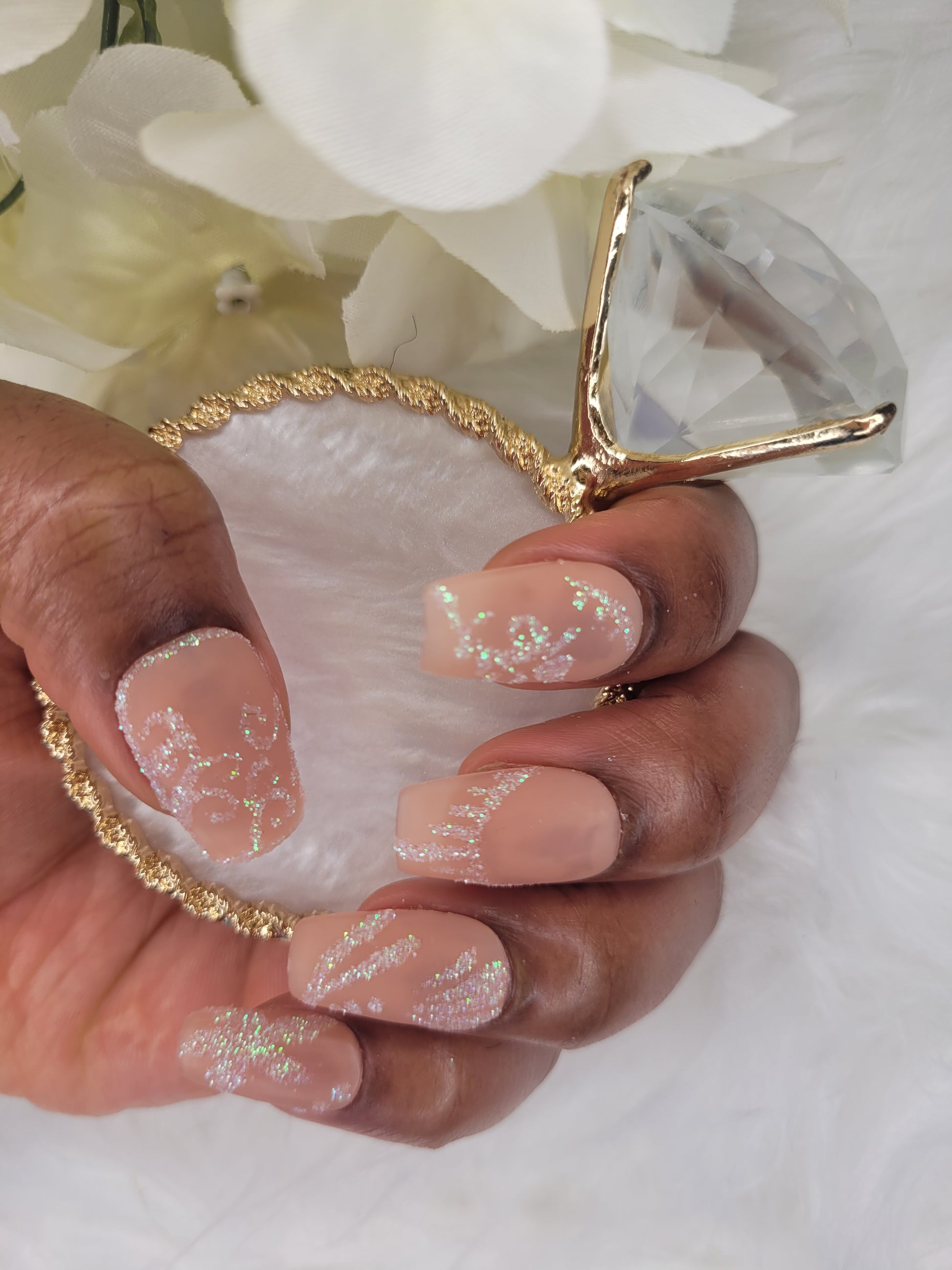 Hand with glittery nail design holding a seashell against a white background