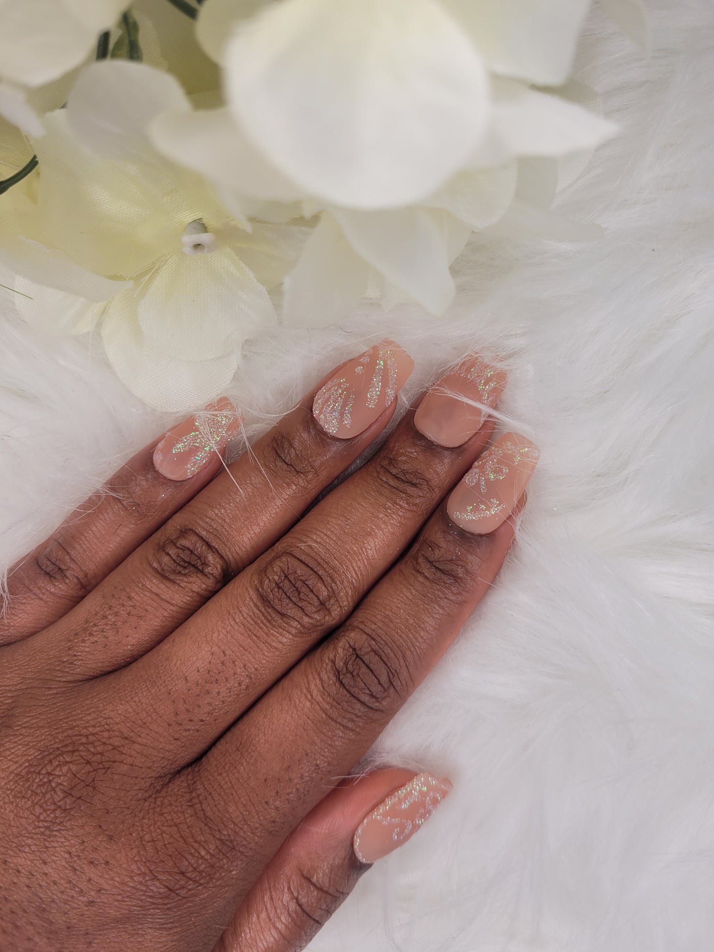 Hand with nude nail polish , glitter design on a white background with flowers